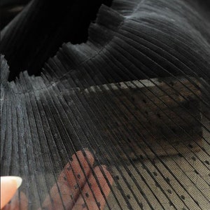 May include: Black pleated tulle fabric with small white polka dots. The fabric is sheer and has a delicate texture.
