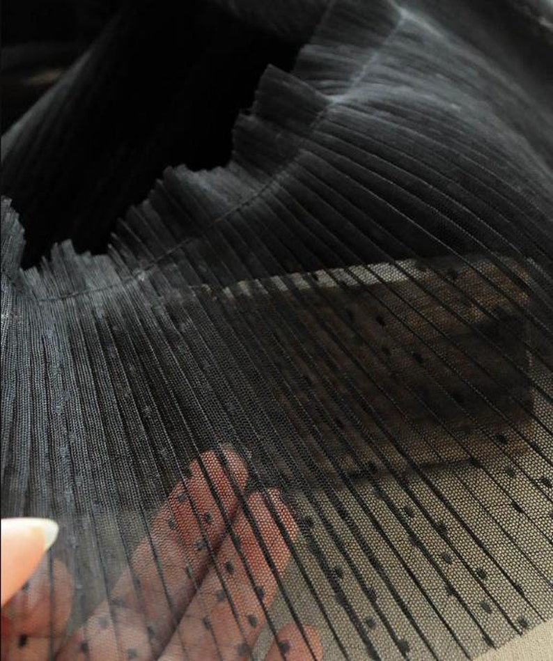 May include: Black pleated tulle fabric with small white polka dots. The fabric is sheer and has a delicate texture.