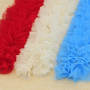 May include: Three strips of ruffled fabric in red, white and light blue. The fabric is soft and delicate, with a slightly sheer texture.