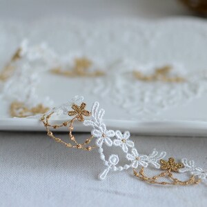 May include: White lace trim with gold accents. The lace features a delicate floral design with small flowers and leaves.