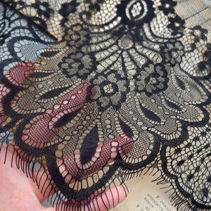 May include: Black lace fabric with a delicate floral pattern. The lace has a scalloped edge and is sheer.