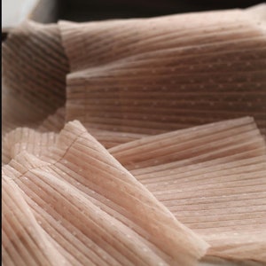 May include: Close-up of a pale pink fabric with a dotted pattern and pleated texture.