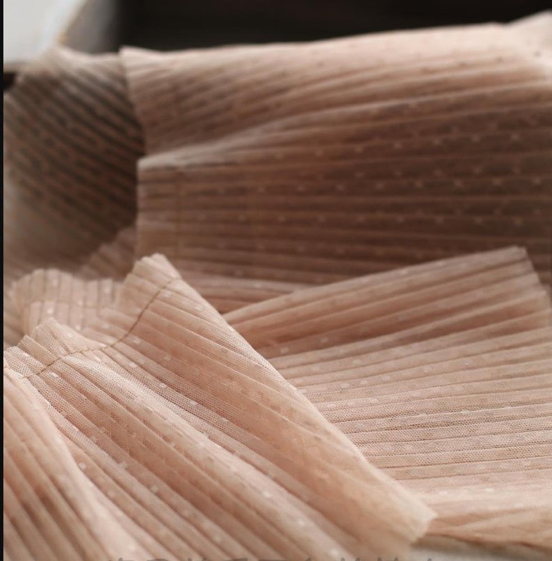 May include: Close-up of a pale pink fabric with a dotted pattern and pleated texture.