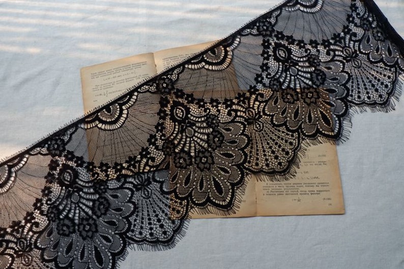 May include: Black lace trim with a scalloped edge and intricate floral patterns. The lace is delicate and has a soft, flowing texture.