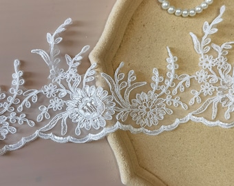 May include: White lace trim featuring a floral design. The lace is delicate and intricate, with small flowers and leaves.