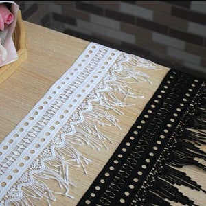 May include: Two pieces of trim with fringe. One is white with a geometric pattern and the other is black with a similar pattern.