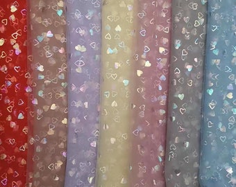Pode incluir: Seis cores diferentes de tecido transparente com um padrão de coração holográfico. As cores são vermelho, rosa, roxo, amarelo, rosa claro e azul.