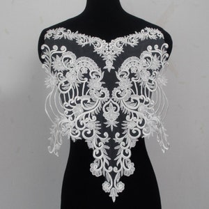 May include: White lace applique with a floral design. The lace is delicate and intricate, with a scalloped edge. This applique would be perfect for adding a touch of elegance to a wedding dress, bridal gown, or other special occasion garment.