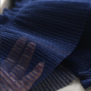 May include: Close-up of navy blue pleated tulle fabric with small white polka dots. The fabric is soft and delicate, with a subtle sheen.