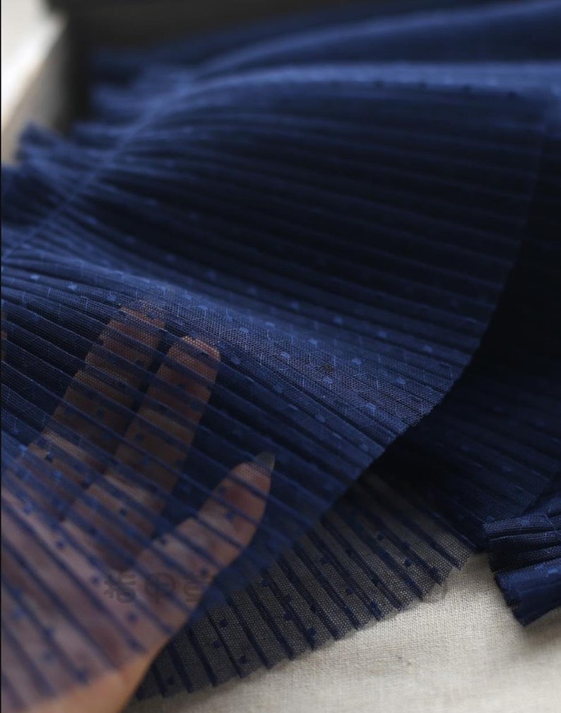 May include: Close-up of navy blue pleated tulle fabric with small white polka dots. The fabric is soft and delicate, with a subtle sheen.