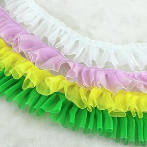 May include: Four layers of ruffled trim in white, pink, yellow, and green. The trim is made of a sheer fabric and is perfect for adding a touch of elegance to any project.