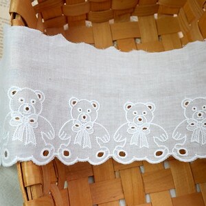 Peut inclure: Bordure en dentelle de coton blanche avec un bord festonn&eacute; et des ours en peluche brod&eacute;s tenant des n&oelig;uds. La dentelle est dans un panier.