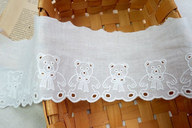 Peut inclure: Bordure en dentelle de coton blanche avec un bord festonn&eacute; et des ours en peluche brod&eacute;s tenant des n&oelig;uds. La dentelle est dans un panier.