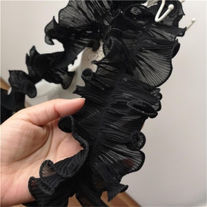 May include: Black ruffled trim with a delicate, sheer texture. The trim is gathered and pleated, creating a soft, flowing look.