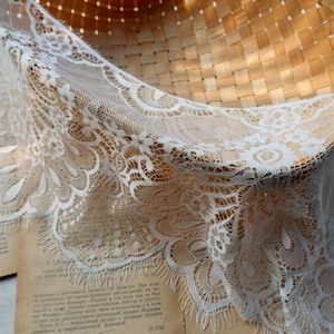 May include: White lace trim with a delicate floral pattern. The lace has a scalloped edge and a frayed fringe.