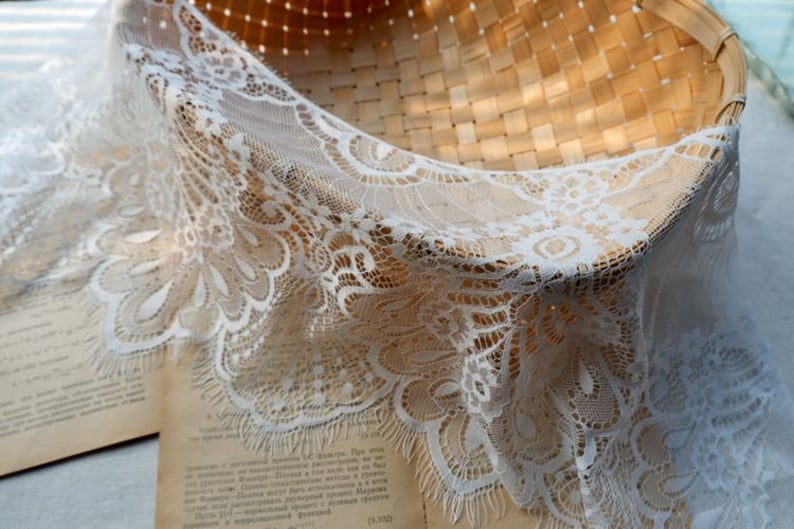 May include: White lace trim with a delicate floral pattern. The lace has a scalloped edge and a frayed fringe.