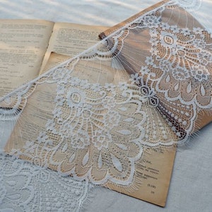 May include: White lace trim with a delicate floral pattern. The lace is draped over a book with a brown cover.