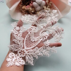 May include: White lace applique with floral and leaf designs, embellished with sequins. The applique is on a sheer mesh fabric.