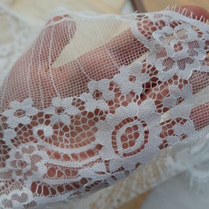 May include: White lace trim with a delicate floral pattern. The lace is soft and sheer, with a scalloped edge.