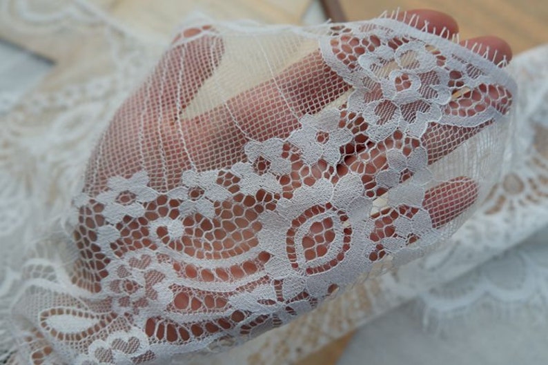 May include: White lace trim with a delicate floral pattern. The lace is soft and sheer, with a scalloped edge.
