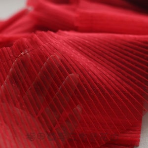 May include: Red pleated mesh fabric with a fine, dotted texture. The fabric is soft and delicate, and it would be perfect for adding a touch of elegance to any project.