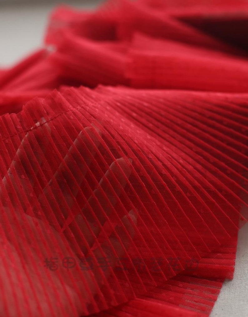 May include: Red pleated mesh fabric with a fine, dotted texture. The fabric is soft and delicate, and it would be perfect for adding a touch of elegance to any project.