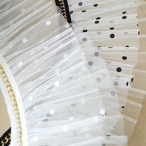 May include: White tulle fabric with black polka dots. The fabric is gathered and ruffled, creating a delicate and feminine look.