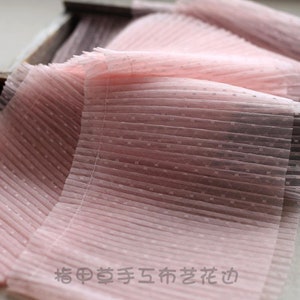 May include: Pink pleated tulle fabric with small white polka dots. The fabric is folded and has a soft, delicate texture.