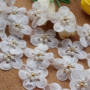 May include: White lace trim with pearl and gold accents. The trim features a repeating pattern of delicate flowers.