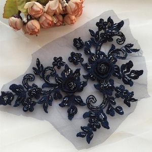 Może przedstawiać: Aplikacja z koronki kwiatowej w kolorze granatowym z ozdobami z koralików. Aplikacja przedstawia delikatny wzór kwiatowy z misternymi detalami i błyszczącymi koralikami.