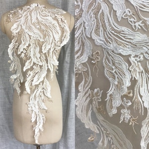 Könnte beinhalten: Weiße Spitzenapplikation mit floralem Muster. Die Spitze ist zart und filigran, mit einem fließenden Muster. Sie ist perfekt, um jedem Kleidungsstück einen Hauch von Eleganz zu verleihen.