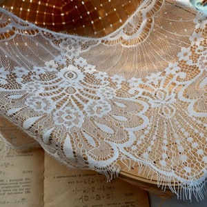 May include: White lace trim with a delicate floral pattern. The lace is soft and flowing, with a scalloped edge. It is perfect for adding a touch of elegance to any project.