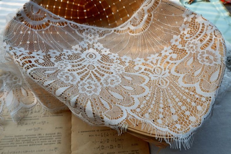 May include: White lace trim with a delicate floral pattern. The lace is soft and flowing, with a scalloped edge. It is perfect for adding a touch of elegance to any project.