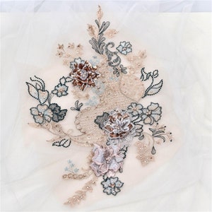 May include: A delicate floral applique with intricate embroidery and sequins. The applique features a variety of flowers in shades of pink, brown, and blue, with pearl-like beads scattered throughout.