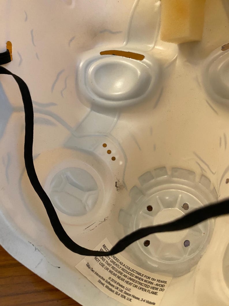 May include: A white plastic mask with a black elastic band. The mask has a detailed design and is intended as a collectible for ages 15 and up. The text on the mask reads: "Recommended as a collectible for 15+ years. Variations that require an unrestricted view do not use or wear near heat or open flame."