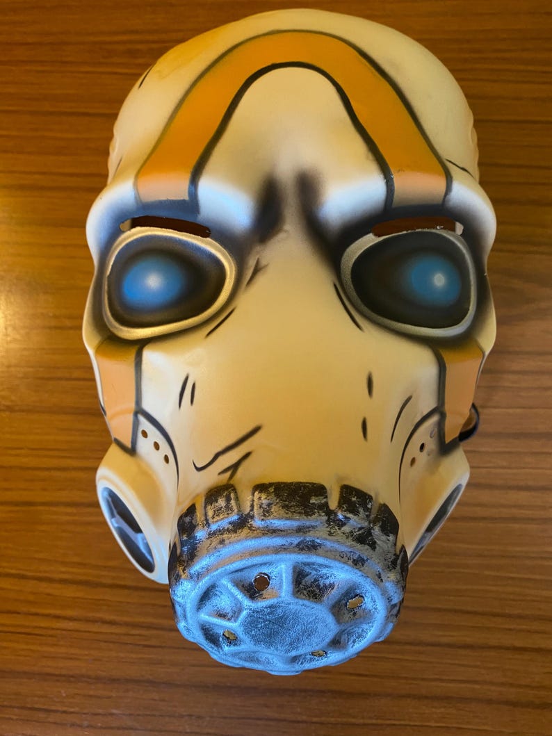 May include: A white plastic mask with orange and black stripes, blue eyes, and a black and gray gas mask mouthpiece.