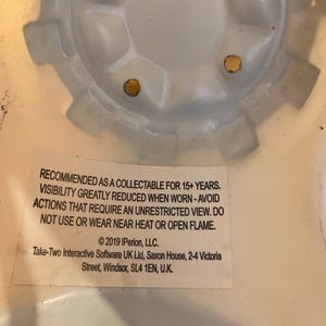 May include: White plastic collectible toy helmet with a warning label that reads: RECOMMENDED AS A COLLECTABLE FOR 15+ YEARS. VISIBILITY GREATLY REDUCED WHEN WORN - AVOID ACTIONS THAT REQUIRE AN UNRESTRICTED VIEW. DO NOT USE OR WEAR NEAR HEAT OR OPEN FLAME. &copy;2019 IPerion, LLC. Take-Two Interactive Software UK Ltd, Saxon House, 2-4 Victoria Street, Windsor, SL4 1EN, U.K.