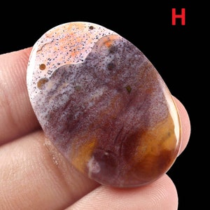 K&ouml;nnte beinhalten: Ein brauner, orangefarbener und wei&szlig;er Achat-Cabochon mit einem wirbelnden Muster. Der Stein ist oval geformt und hat eine glatte, polierte Oberfl&auml;che.
