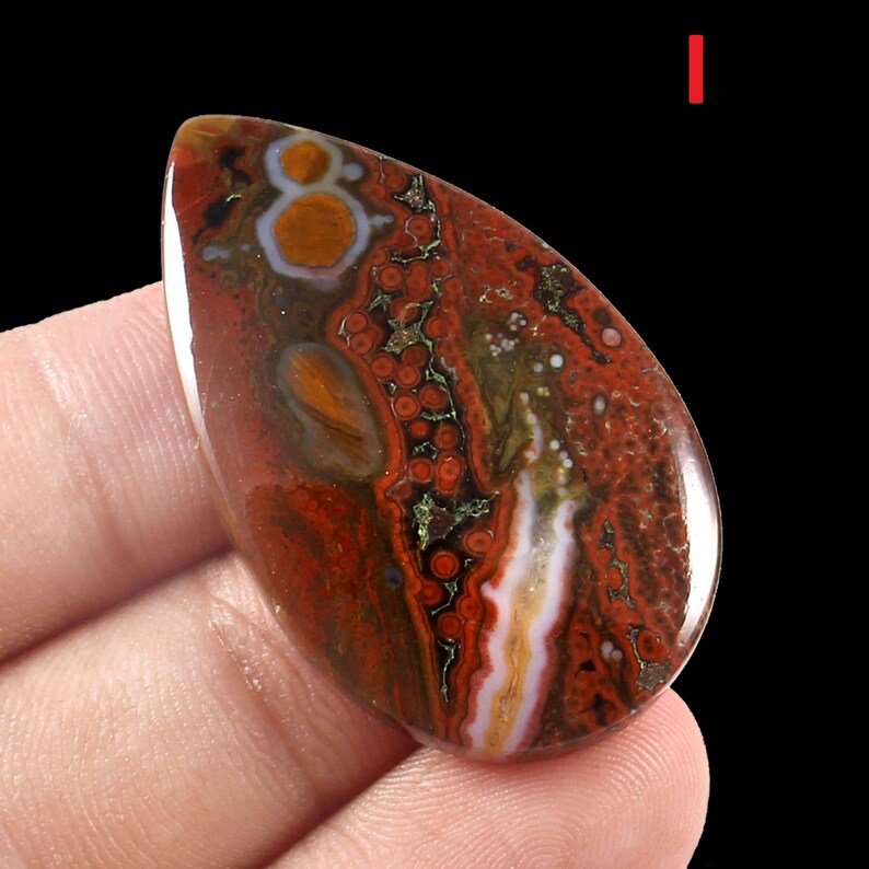 K&ouml;nnte beinhalten: Ein tropfenf&ouml;rmiger, rot-braun-wei&szlig;er Achat-Cabochon mit komplizierten Mustern und Wirbeln. Der Stein hat eine polierte Oberfl&auml;che und ist in einer silbernen Fassung gefasst.