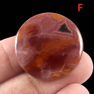 K&ouml;nnte beinhalten: Ein runder, rot-orangefarbener Achat-Cabochon mit einem dunkelgr&uuml;nen und schwarzen Muster. Der Cabochon ist poliert und hat eine glatte Oberfl&auml;che.