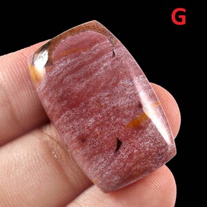 K&ouml;nnte beinhalten: Ein rechteckiger Cabochon aus rotem, wei&szlig;em und goldenem Edelstein. Der Stein hat ein wirbelndes Muster und eine glatte, polierte Oberfl&auml;che.