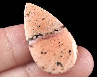 Könnte beinhalten: Ein tropfenförmiger Cabochon aus rosa und braunem Achat mit einem weißen und schwarzen Bandmuster. Der Stein hat eine gesprenkelte Textur.