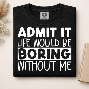 May include: A black short-sleeved t-shirt with a white graphic print that reads ADMIT IT LIFE WOULD BE BORING WITHOUT ME. The shirt features a Comfort Colors brand label at the inner neckline, indicating a size small, and is made of cotton.