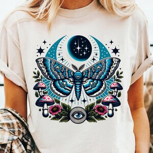May include: White t-shirt with a blue and white moth, crescent moon, stars, mushrooms, and an all-seeing eye graphic.