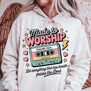May include: A white hoodie with a pink and blue cassette tape graphic. The text on the hoodie reads "Made to Worship" and "Let everything that has breath praise the Lord".
