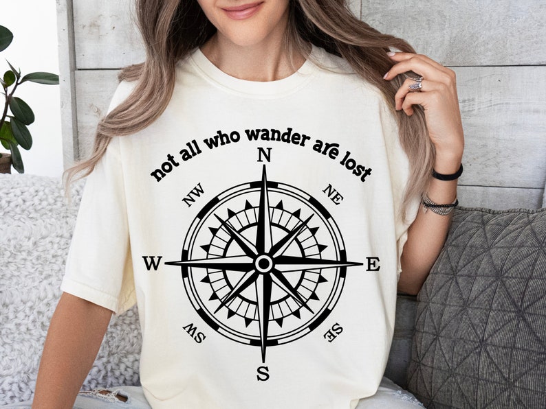 May include: A white t-shirt with the text "not all who wander are lost" and a compass graphic with the directions N, NE, E, SE, S, SW, W, NW.