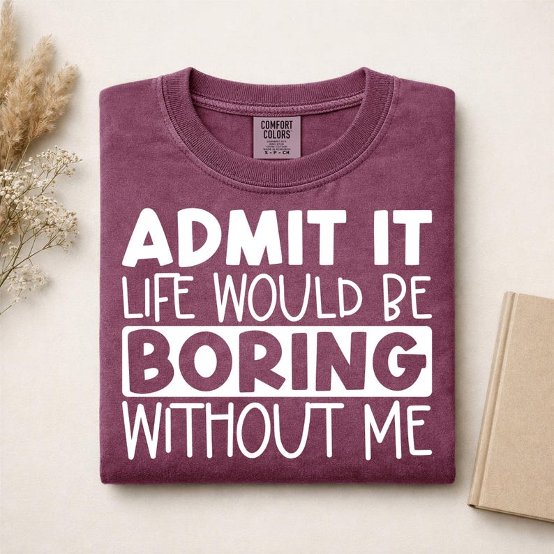 May include: A maroon crewneck t-shirt featuring the white text "ADMIT IT LIFE WOULD BE BORING WITHOUT ME" printed on the front. The shirt has a Comfort Colors brand label inside the collar and a ribbed neckline.