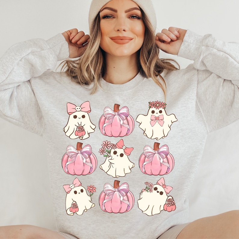 K&ouml;nnte beinhalten: Ein hellgraues Sweatshirt mit Rundhalsausschnitt und einem Raster aus neun Illustrationen. Das Design zeigt wei&szlig;e Geister mit rosa Schleifen und Blumen sowie rosa K&uuml;rbisse, die mit gro&szlig;en, detaillierten rosa-wei&szlig;en B&auml;ndern verziert sind.