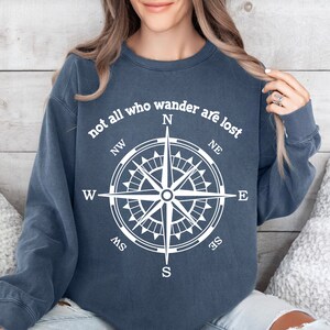 May include: A navy blue sweatshirt with the text "not all who wander are lost" and a compass graphic in white.