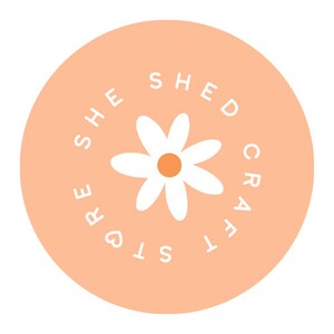 May include: A peach-colored circle with the text "She Shed Crafts" in white, surrounding a white daisy with a yellow center.